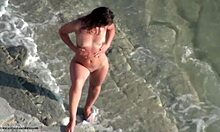 Une brune épaisse se promène sur une plage nudiste totalement nue