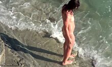Wanita berambut coklat tebal berjalan-jalan di pantai nudis yang benar-benar telanjang