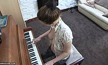 Játékos külsejű barna hajú lány hetyke mellekkel játszik a zongorán, félmeztelenül